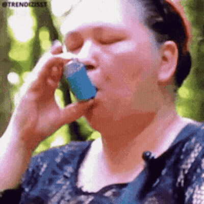 A Woman Is Talking On A Cell Phone While Holding A Blue Asthma Inhaler In Her Mouth . GIF