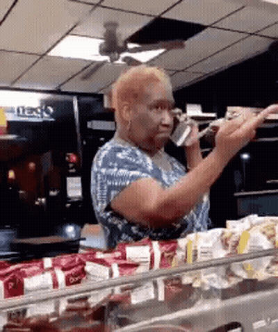 A Woman Is Talking On A Cell Phone While Standing In Front Of A Counter . GIF
