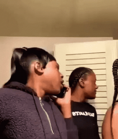 A Woman Is Talking On A Cell Phone While Standing Next To Another Woman In A Room . GIF