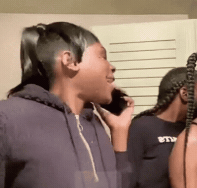 A Woman Is Talking On A Cell Phone While Standing Next To Another Woman In A Room . GIF