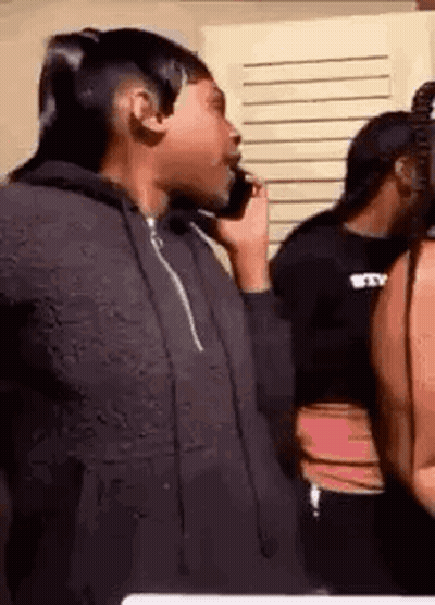 A Woman Is Talking On A Cell Phone While Standing Next To Another Woman . GIF