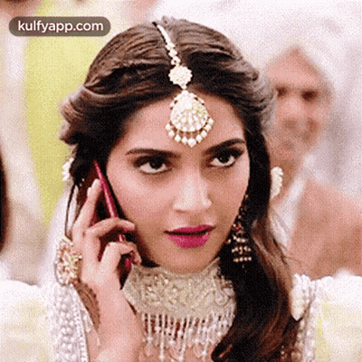 A Woman Is Talking On A Cell Phone While Wearing A Headpiece . GIF