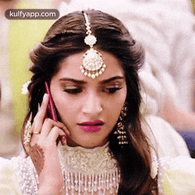A Woman Is Talking On A Cell Phone While Wearing A Headpiece And Earrings . GIF
