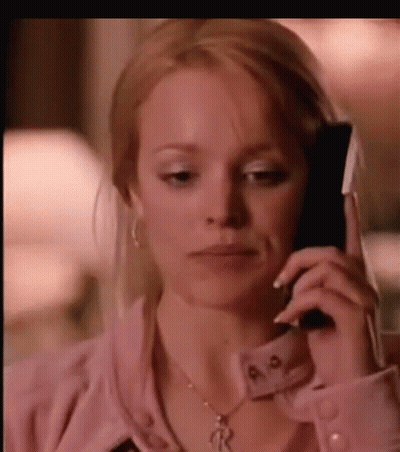 A Woman Is Talking On A Cell Phone While Wearing A Pink Shirt And A Necklace . GIF