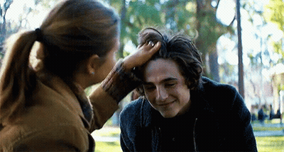 A Woman Is Touching A Young Man 'S Head In A Park . GIF