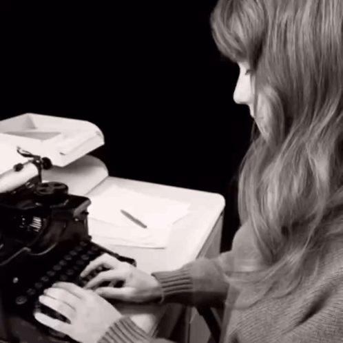 A Woman Is Typing On An Old Typewriter With A Pen In Her Hand GIF