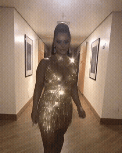 A Woman Is Walking Down A Hallway Wearing A Gold Dress GIF
