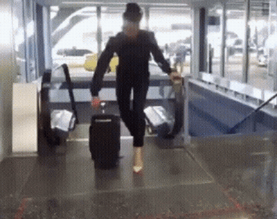 A Woman Is Walking Down A Hallway With A Suitcase On Her Feet GIF