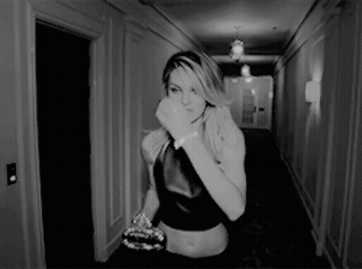 A Woman Is Walking Down A Hallway With Her Hand On Her Face GIF