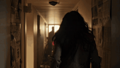 A Woman Is Walking Down A Hallway With Newspapers Hanging On The Walls GIF