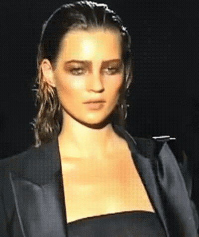A Woman Is Walking Down A Runway Wearing A Black Jacket And A Black Dress . GIF