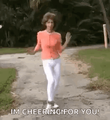 A Woman Is Walking Down A Sidewalk And Waving . GIF