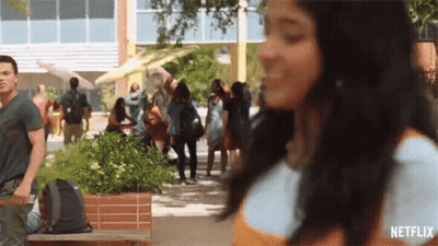 A Woman Is Walking Down A Sidewalk In Front Of A Crowd Of People And A Netflix Logo . GIF