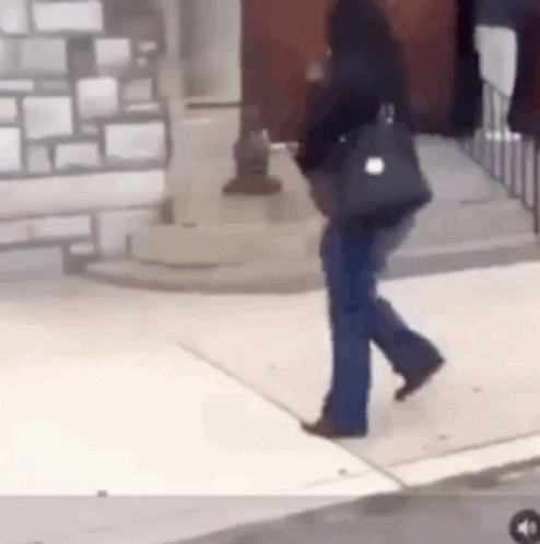 A Woman Is Walking Down A Sidewalk With A Purse On Her Shoulder . GIF