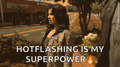 A Woman Is Walking Down A Sidewalk With The Words Hotflashing Is My Superpower GIF
