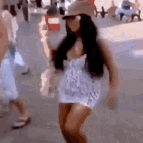 A Woman Is Walking Down A Street Wearing A Hat And Sunglasses . GIF