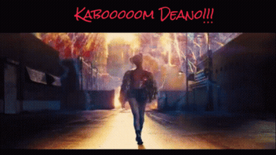 A Woman Is Walking Down A Street With The Words Kabooooom Deano !!! Written On The Bottom GIF