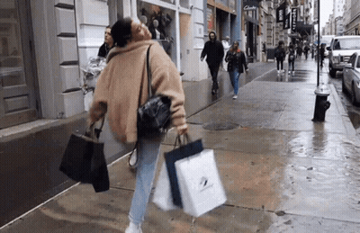 A Woman Is Walking Down The Street Carrying Shopping Bags GIF