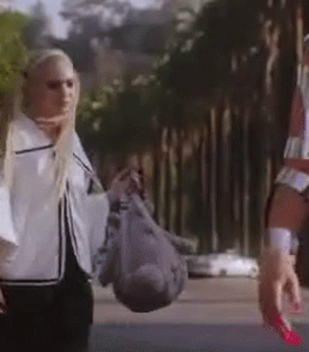 A Woman Is Walking Down The Street Holding A Bag Of Groceries . GIF
