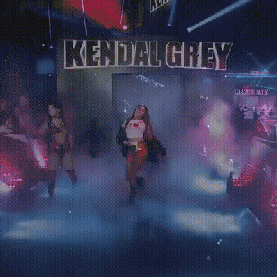 A Woman Is Walking On A Stage In Front Of A Sign That Says Kendall Grey . GIF