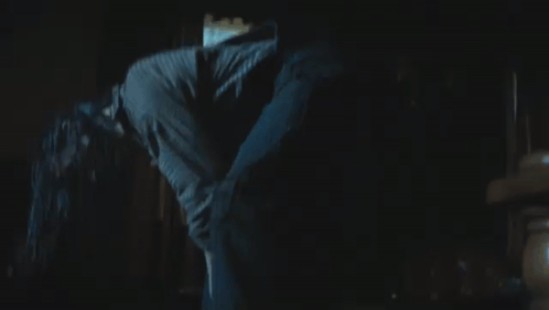 A Woman Is Walking Through A Dark Room With A Window Behind Her GIF