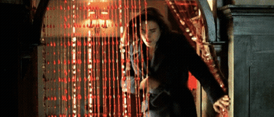 A Woman Is Walking Through A Doorway With A Red Curtain Behind Her . GIF