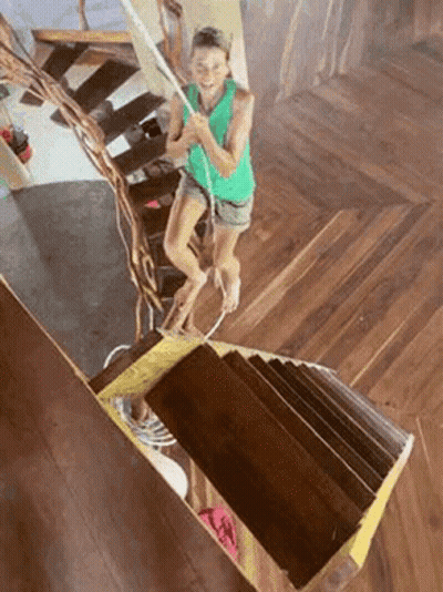 A Woman Is Walking Up A Set Of Wooden Stairs . GIF