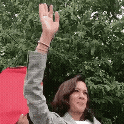 A Woman Is Waving Her Hand In Front Of A Tree . GIF