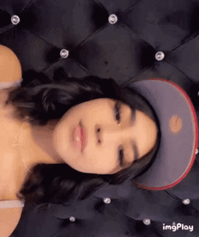 A Woman Is Wearing A Baseball Cap And Laying On A Bed . GIF
