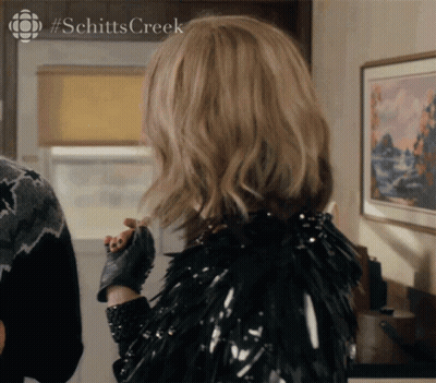A Woman Is Wearing A Black Jacket And Gloves With #Schitts Creek On The Bottom GIF