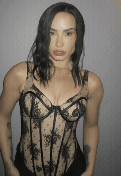 A Woman Is Wearing A Black Lace Bodysuit With A Plunging Neckline GIF