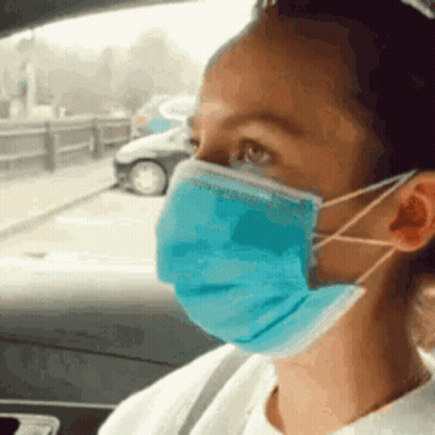 A Woman Is Wearing A Blue Face Mask While Sitting In A Car . GIF