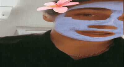 A Woman Is Wearing A Blue Mask On Her Face With A Pink Flower In Her Hair . GIF