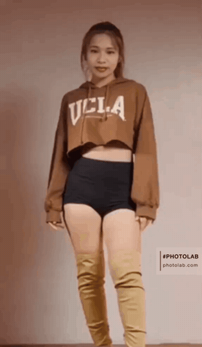A Woman Is Wearing A Brown Ucla Hoodie And Black Shorts GIF