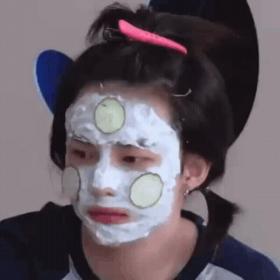 A Woman Is Wearing A Face Mask With Cucumber Slices On It . GIF