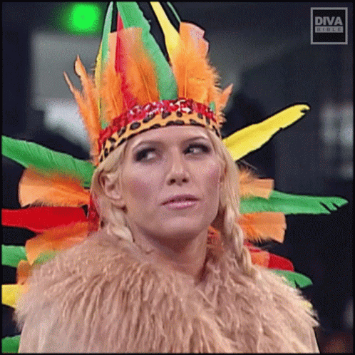 A Woman Is Wearing A Feathered Headdress And A Fur Coat With Diva Written On The Bottom GIF