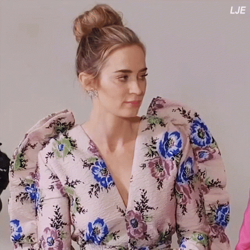 A Woman Is Wearing A Floral Dress With Puffed Sleeves And A Bun In Her Hair GIF