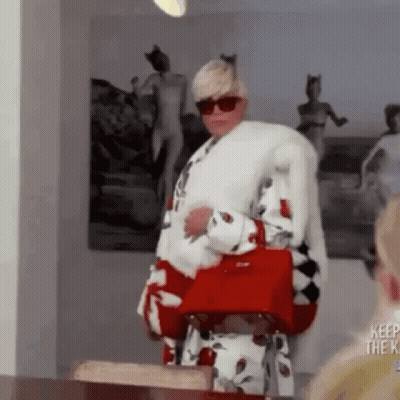 A Woman Is Wearing A Fur Coat And Holding A Red Purse . GIF