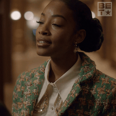 A Woman Is Wearing A Green Jacket And A White Shirt With A Be Logo In The Background GIF