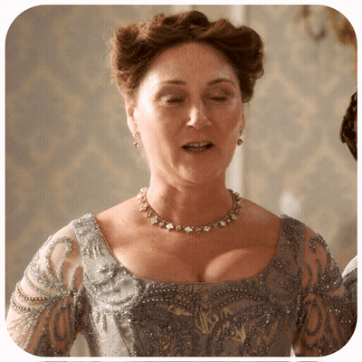 A Woman Is Wearing A Necklace And Earrings And A Gray Dress GIF