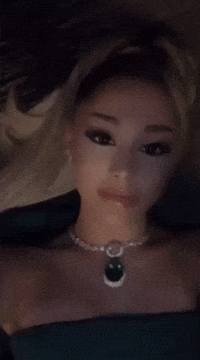 A Woman Is Wearing A Necklace With A Green Pendant GIF