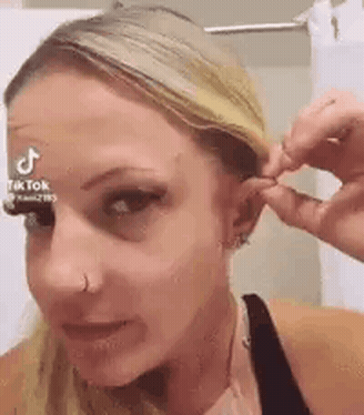 A Woman Is Wearing A Nose Ring And A Nose Ring While Holding Her Hair . GIF