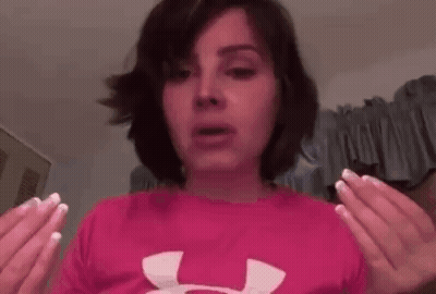 A Woman Is Wearing A Pink Under Armour Shirt And Holding Her Hands Up In The Air . GIF