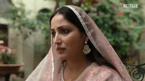A Woman Is Wearing A Pink Veil And Earrings And Looking At The Camera . GIF
