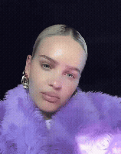 A Woman Is Wearing A Purple Fur Coat And Earrings . GIF