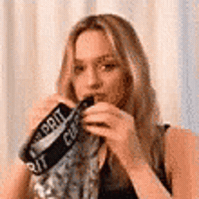 A Woman Is Wearing A Scarf Around Her Neck And Holding A Bottle Of Soda . GIF