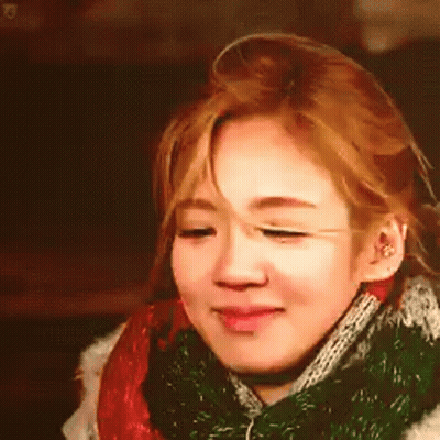 A Woman Is Wearing A Scarf Around Her Neck And Smiling . GIF