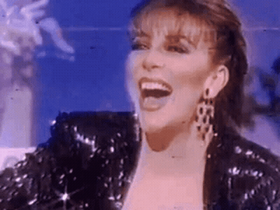 A Woman Is Wearing A Sequined Jacket And Earrings And Laughing . GIF