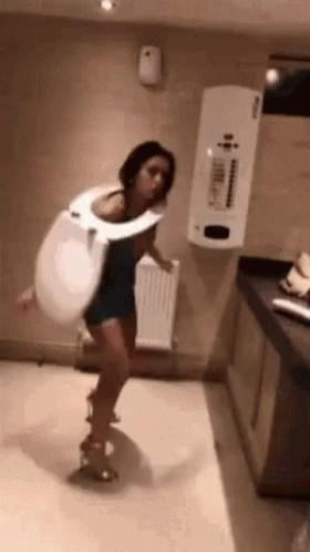 A Woman Is Wearing A Toilet Seat Costume And Dancing In A Bathroom . GIF