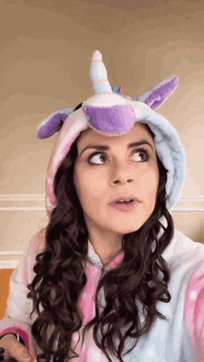 A Woman Is Wearing A Unicorn Costume With A Purple Horn On Her Head . GIF